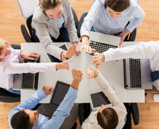 Une équipe au travail autour d'une table qui font en high five. Représente le travail collaboratif